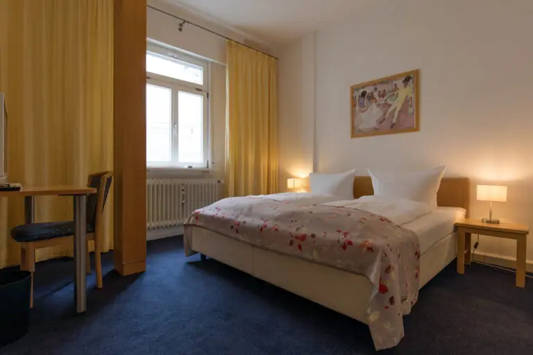 Standard double room with double bed, bedside lamps and yellow curtains